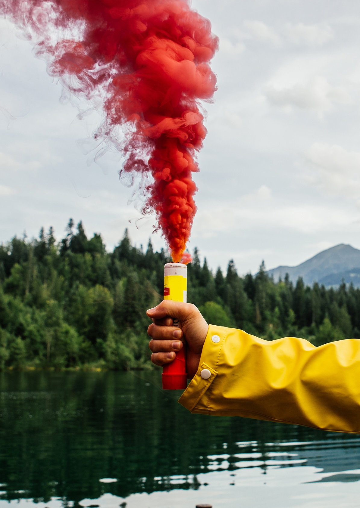 A hand holding an activated red distress flare emitting red smoke