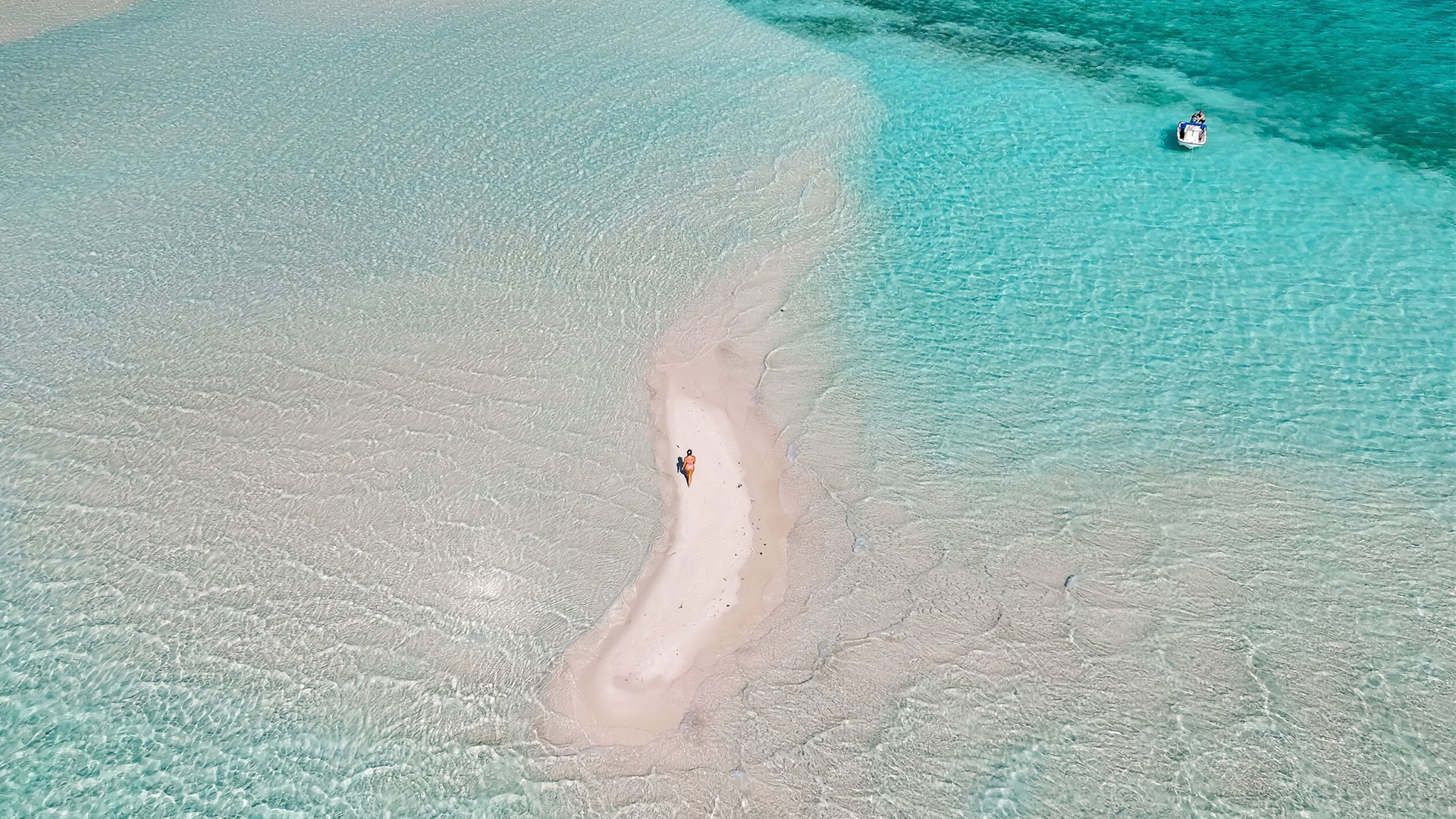 An aerial view of a sandbar at low tide with a small figure walking on it