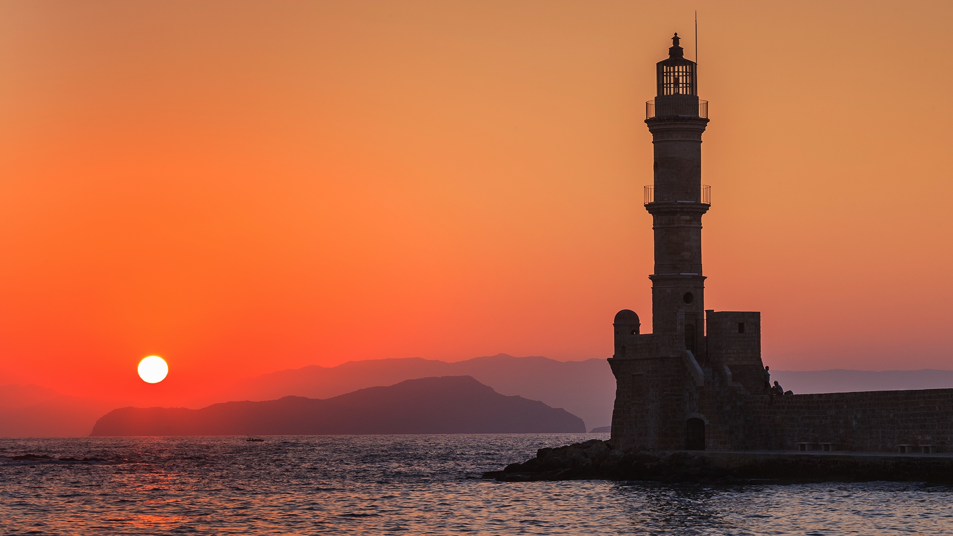 Vista de la entrada a un canal con un pequeño faro al atardecer rojizo