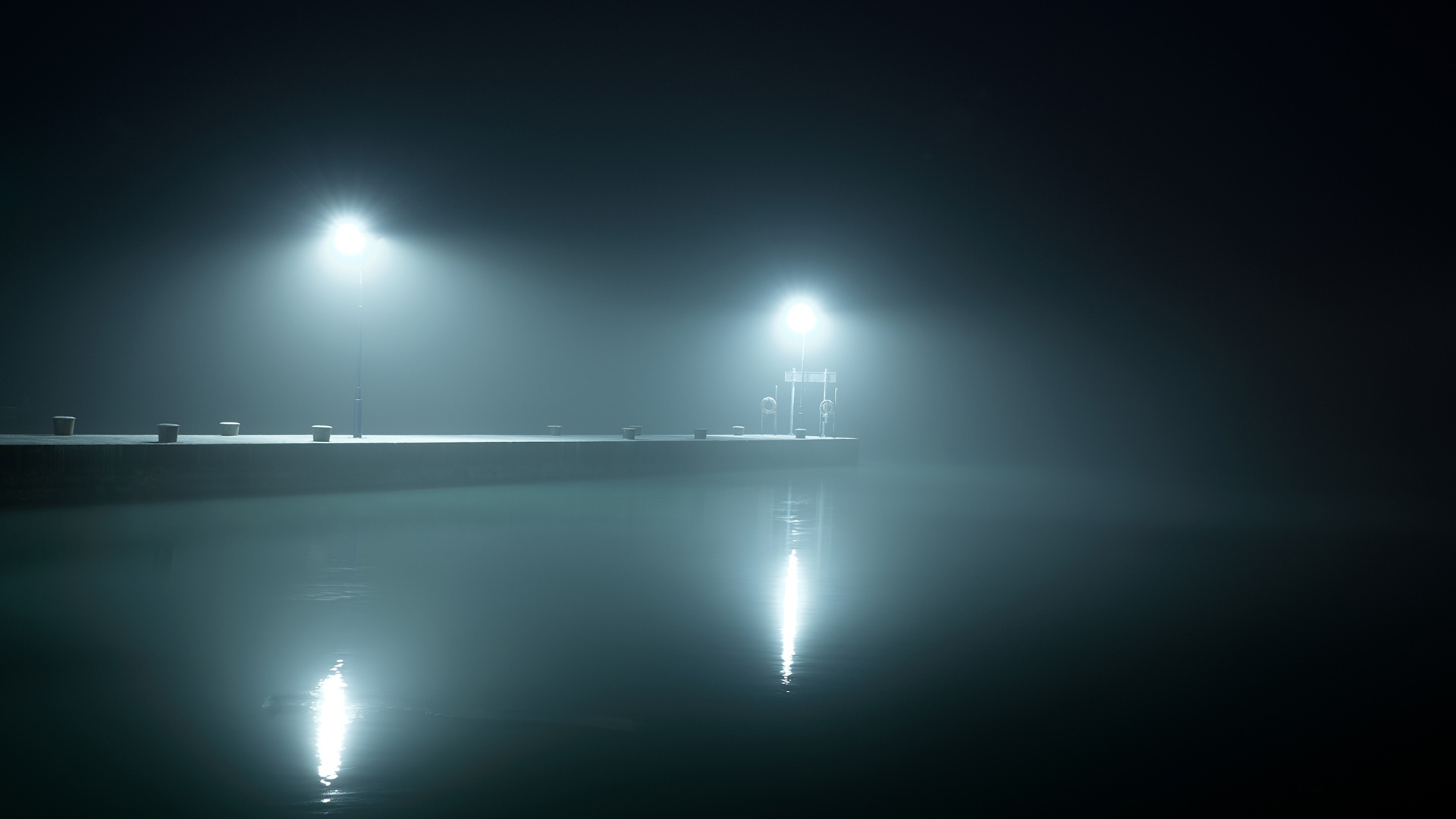 Vista desde el agua de un muelle vacío con dos luces blancas que lo iluminan entre la niebla