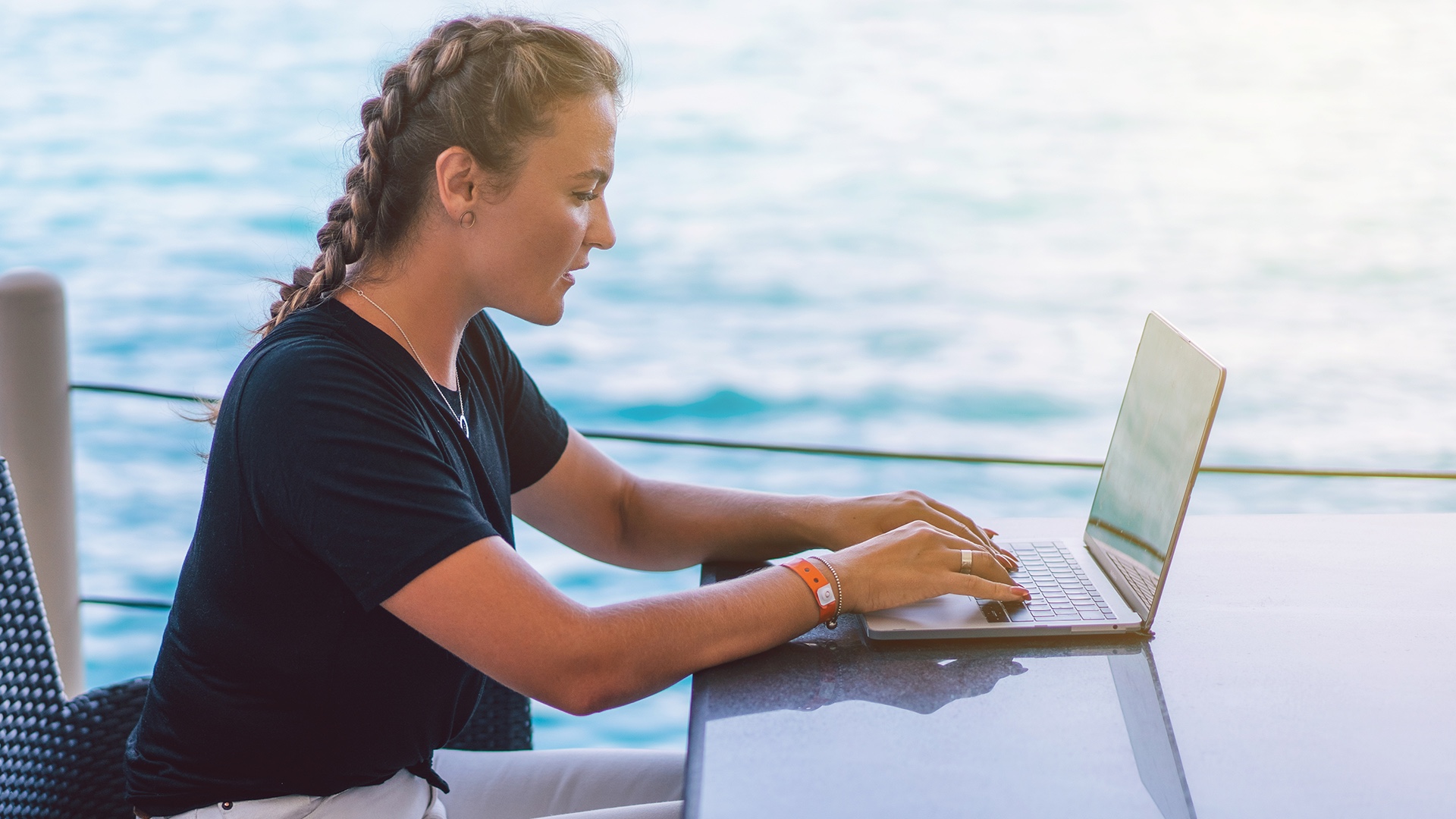 Una mujer trabajando en una laptop a bordo de un yate con el océano de fondo