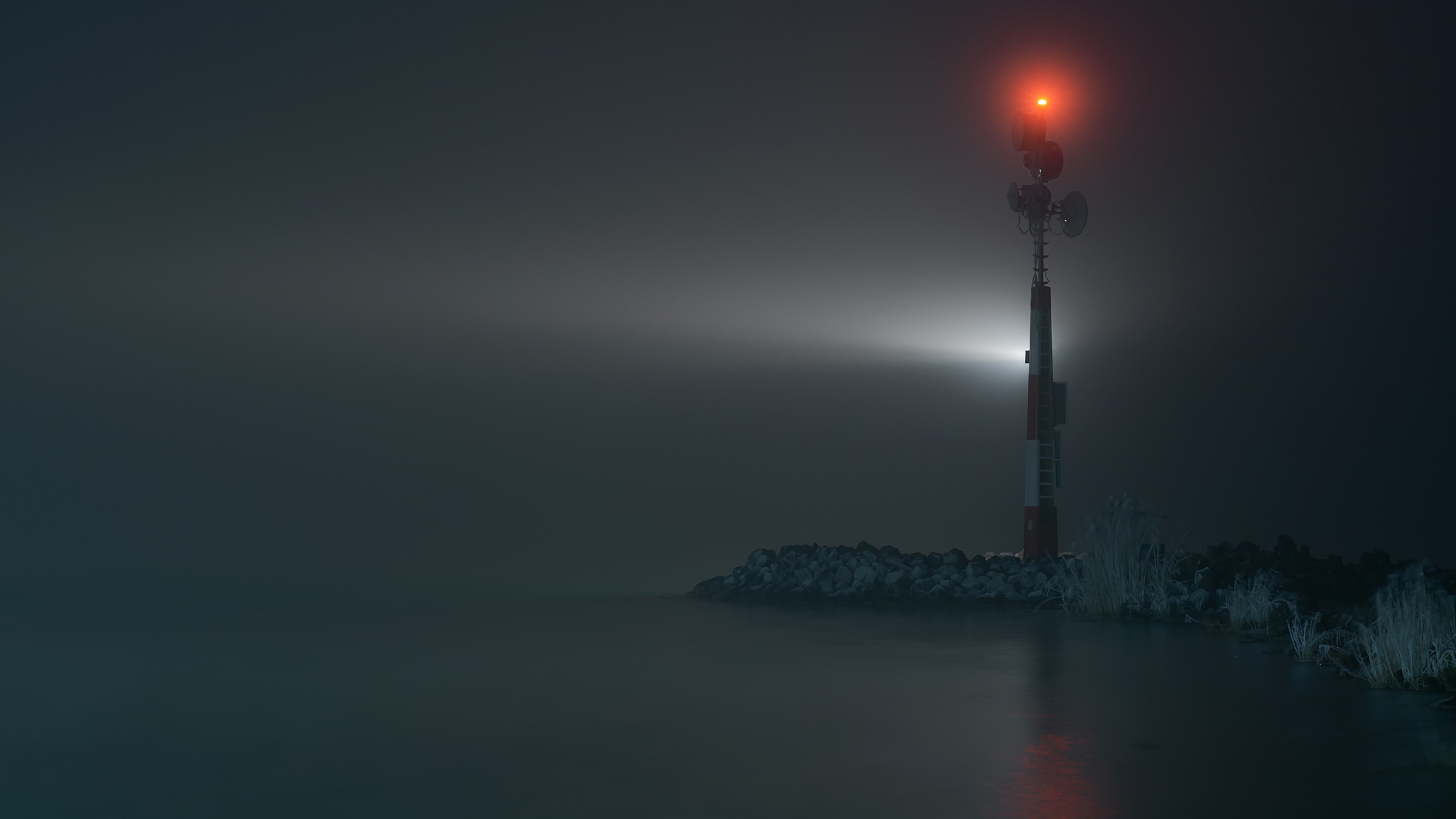 Pequeño faro de entrada a un canal de noche con algo de niebla, vista desde el agua