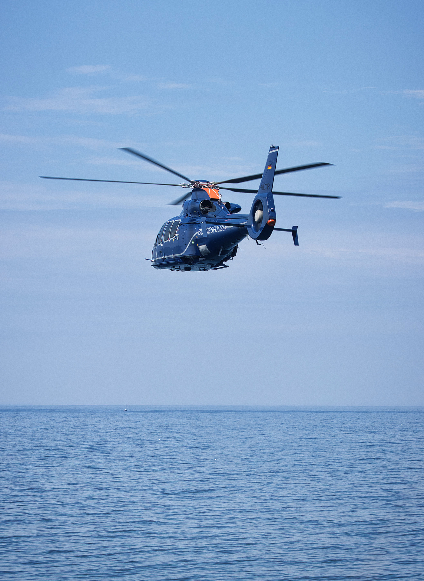 Helicóptero moderno visto en perfil trasero a tres cuartos, volando bajo sobre el agua