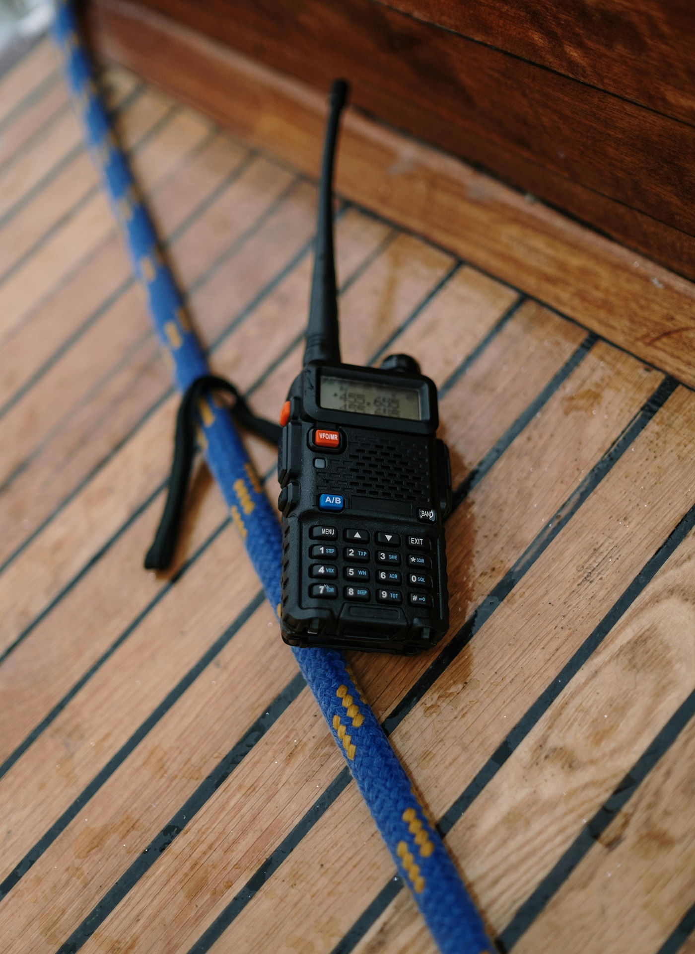 A handheld VHF radio resting on a teak deck
