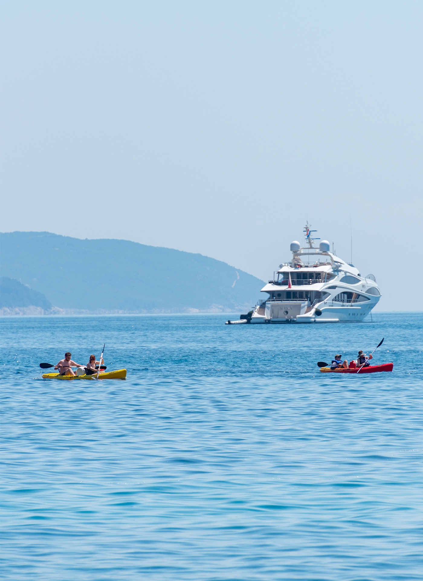 Stern of an anchored superyacht with two kayaks in front