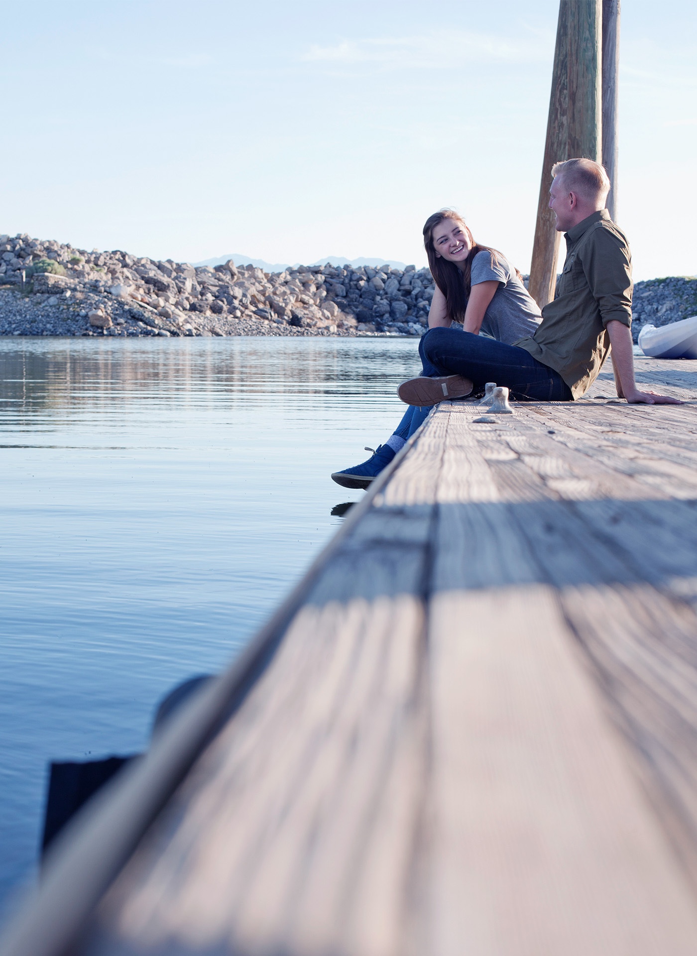 Side view of a couple sitting on a wooden pier by the water