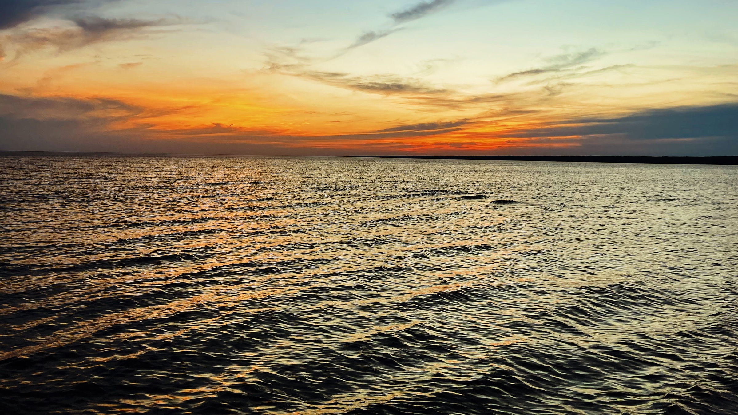 Sunset over a bay with an undeveloped shoreline on the horizon