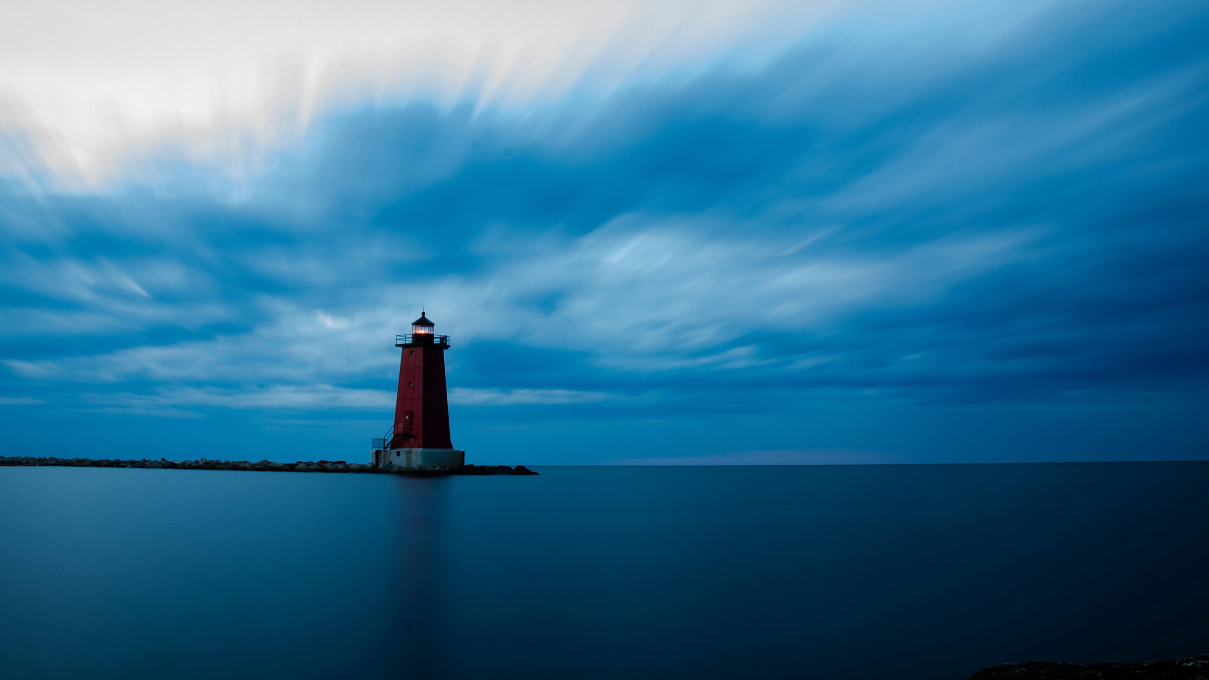Lighthouse at the tip of a peninsula under a streaked, misty sky