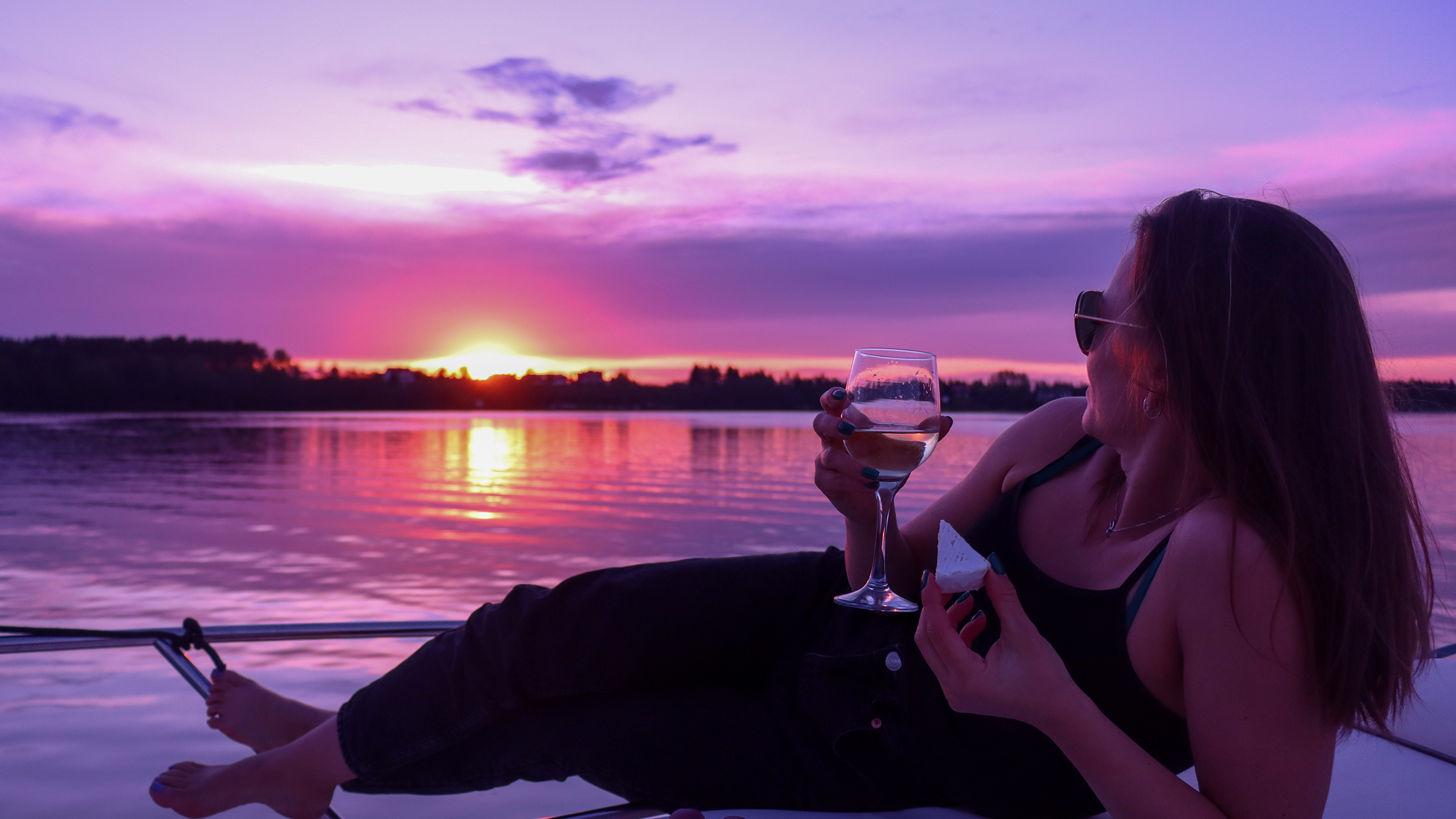 Mujer recostada en el lounge de proa con brie y una copa de vino blanco