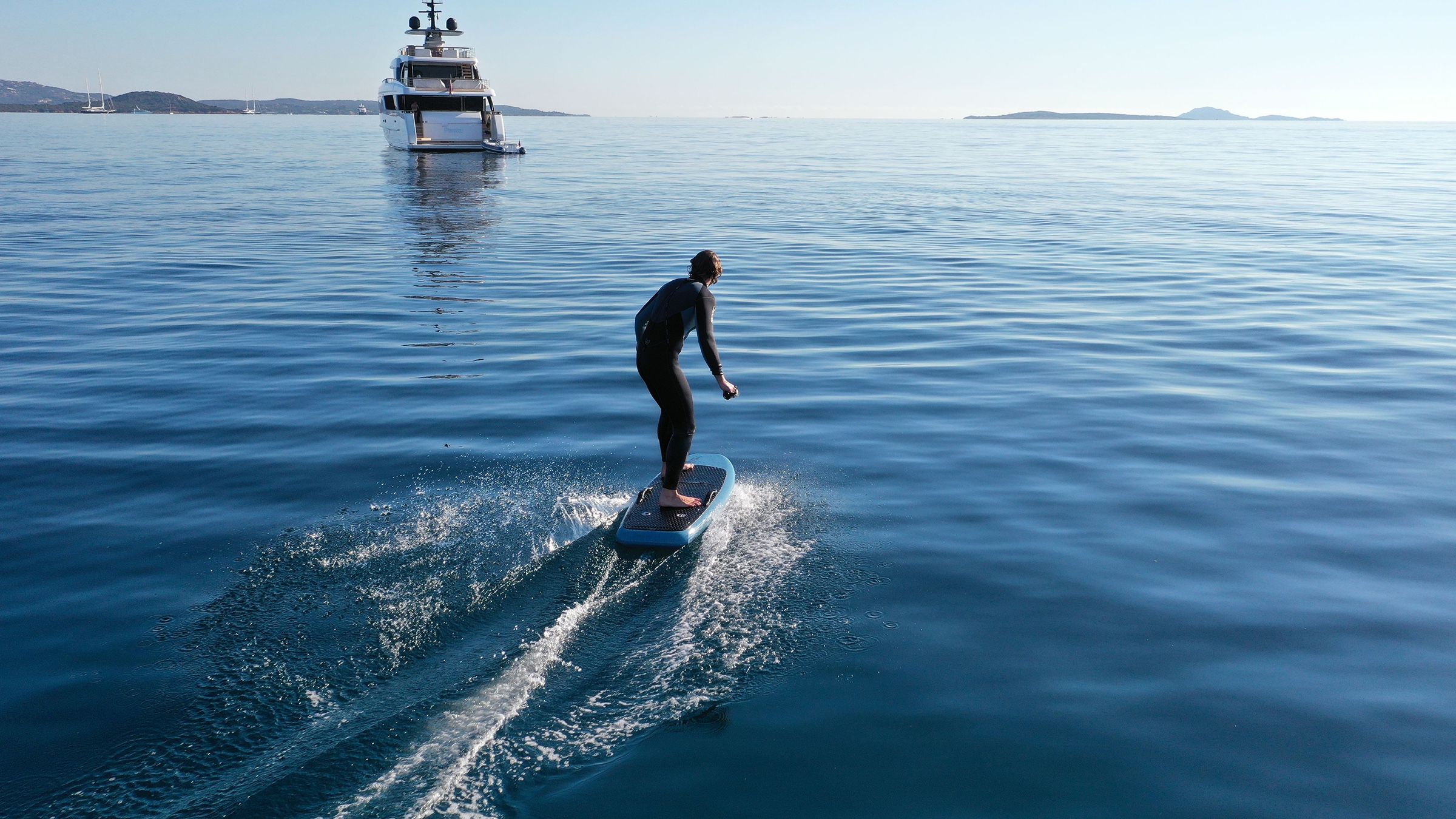 Man on an electric surfboard heading to a yacht's stern