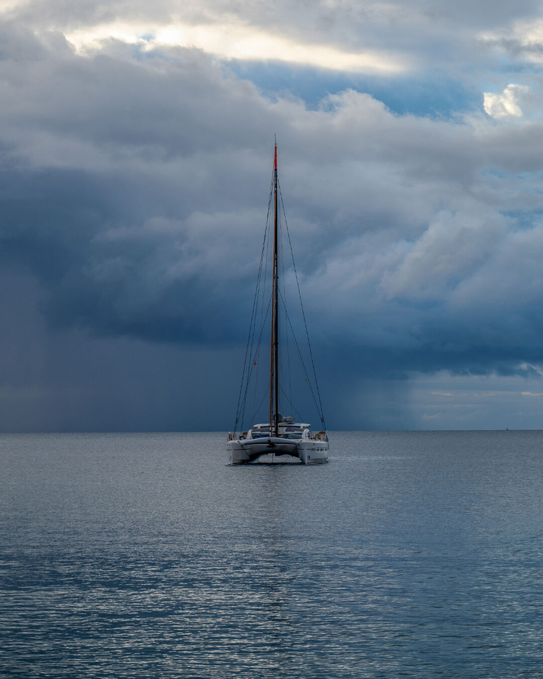 Un velero fondeado en aguas calmas mientras se acerca una gran tormenta por detrás