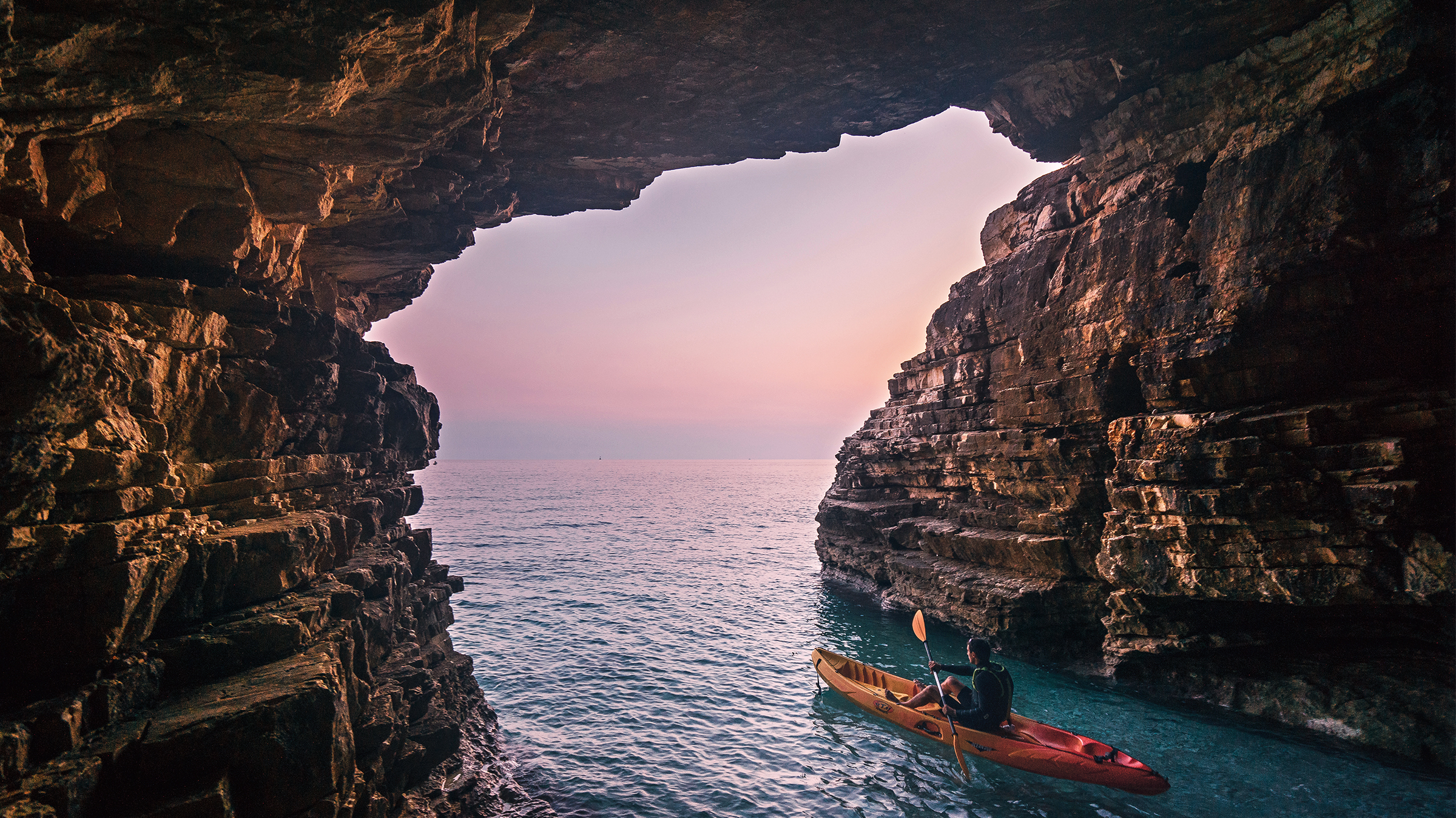 A sea cave at dusk with a kayak emerging into blue water