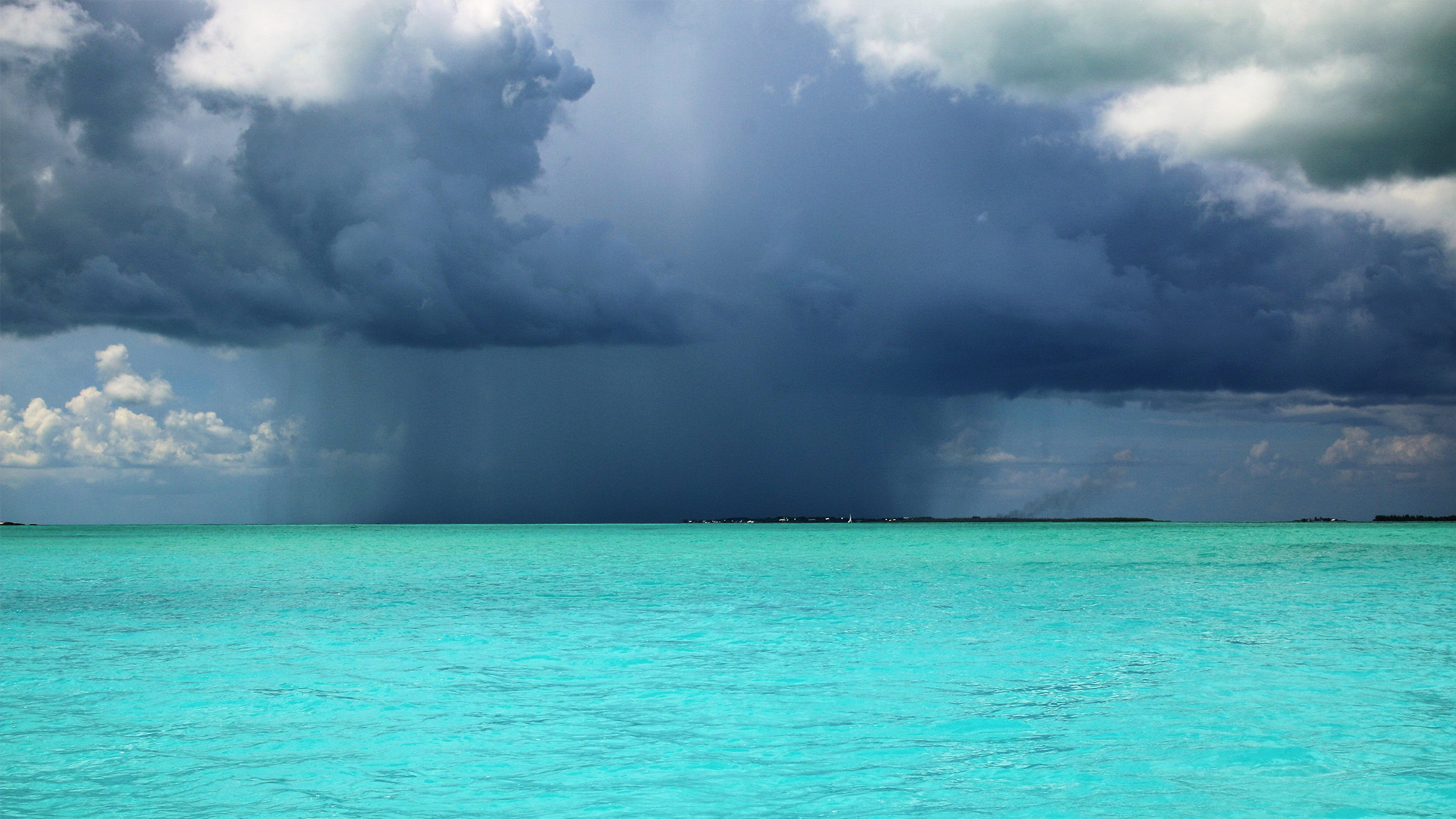 Mar turquesa en calma con una tormenta formándose en el horizonte