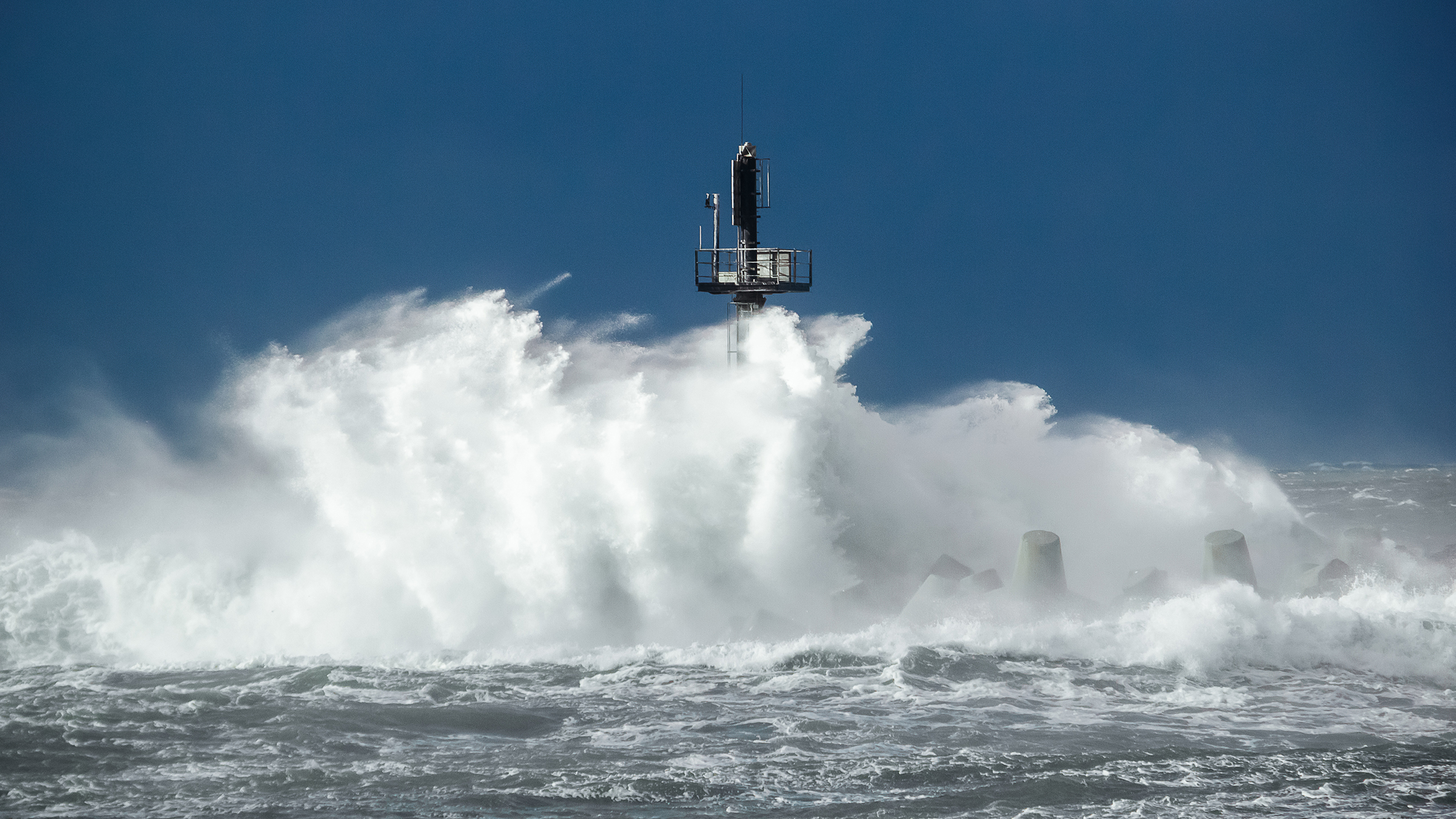 Una gran ola rompiendo contra la torre de entrada a un puerto