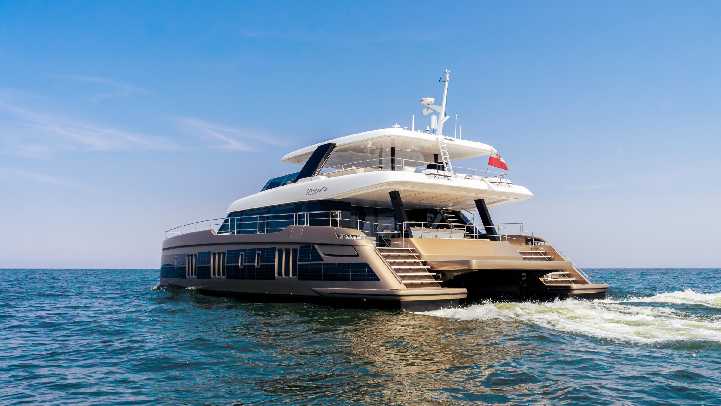 Stern view of the 80 Sunreef Power Eco underway, leaving a wake under a blue sky