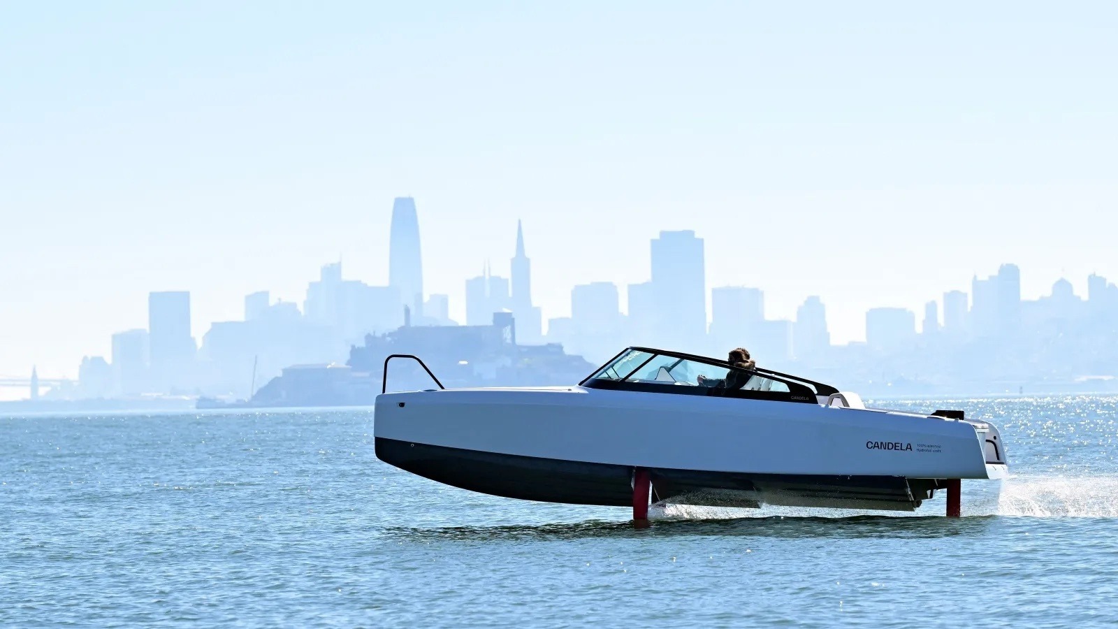 Electric boat with hydrofoils riding above the water in front of a city
