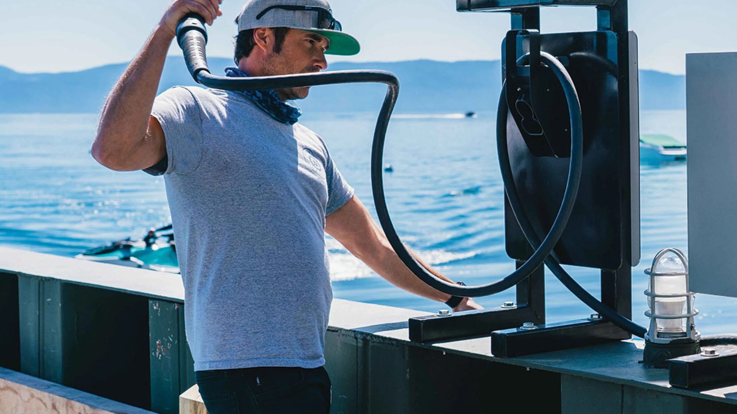 Man picking up the cable of an electric charger on a dock by a lake