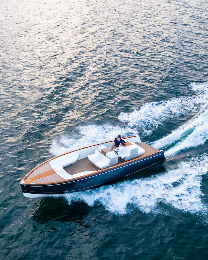 Aerial view of a classic boat with a blue hull and wooden deck, two people aboard