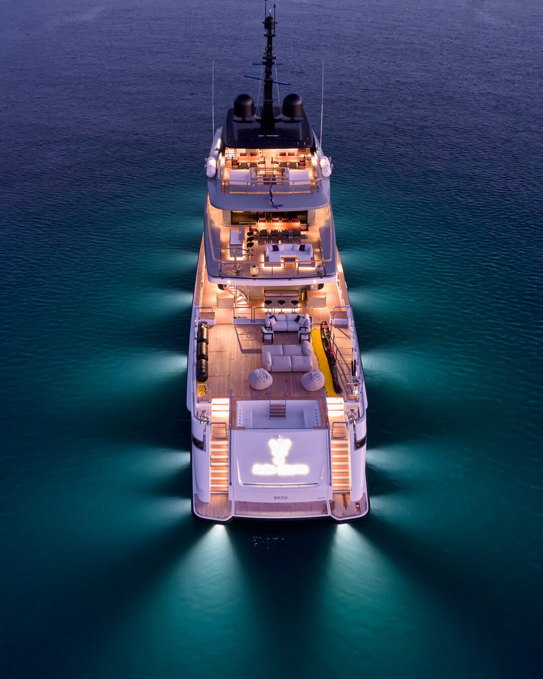 Aerial night view of a superyacht lit by underwater lights